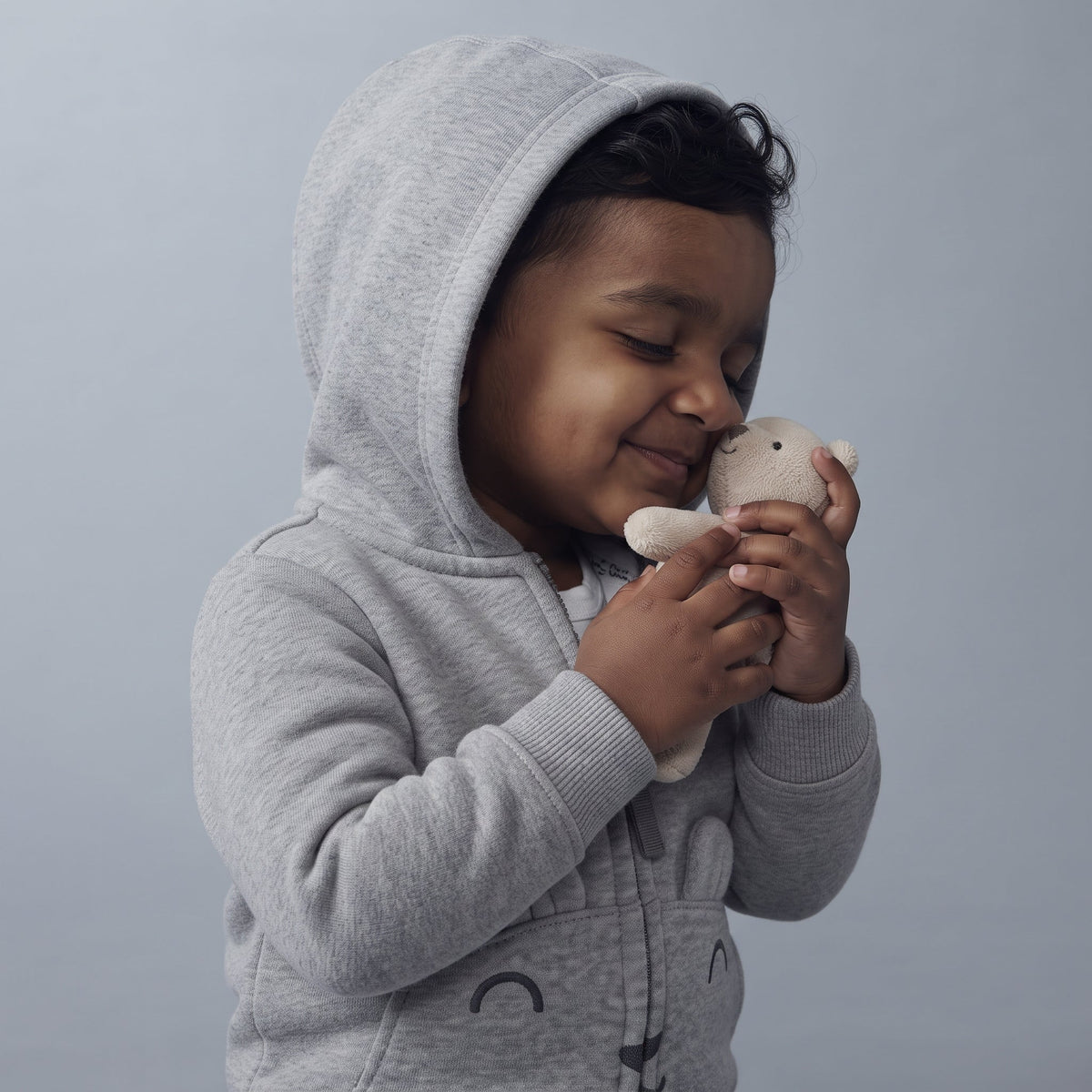 Niño pequeño con chaqueta gris con capucha de EmpiBy abrazando un osito de peluche, estilo tierno y abrigado