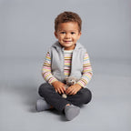 Niño pequeño con conjunto EmpiBy de 3 piezas: chaleco gris con capucha, body a rayas y pantalón jean oscuro.