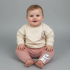 Bebé sonriente vistiendo conjunto EmpiBy de sudadera marfil y legging rosa acanalado con estampado de Marie Disney
