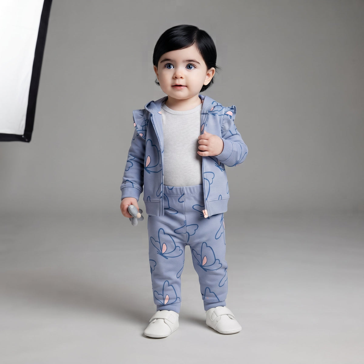 Bebé niña vistiendo conjunto EmpiBy de 3 piezas azul con estampado de mariposas, chaqueta con capucha y leggings.