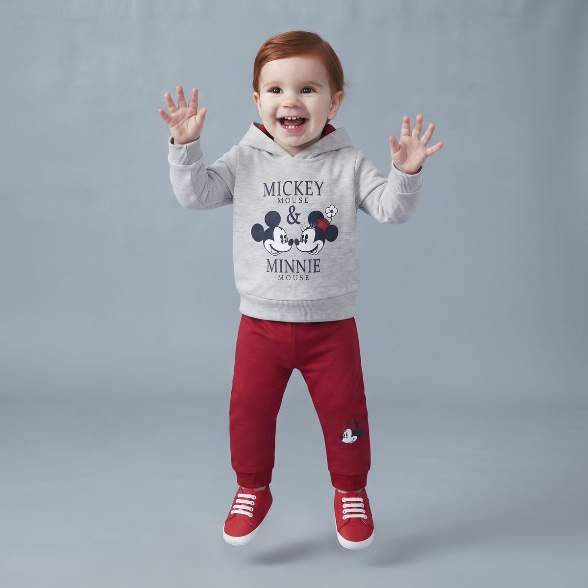 Bebé feliz vistiendo conjunto EmpiBy de sudadera gris con capucha de Mickey y Minnie y pantalón rojo de algodón