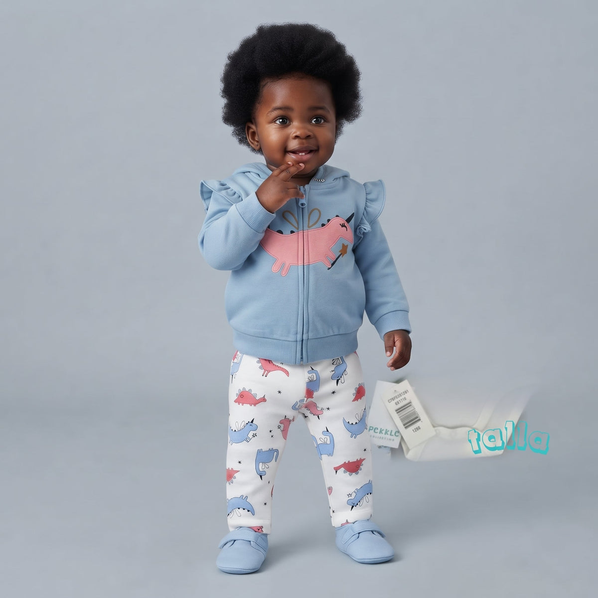 Bebé niña vistiendo conjunto EmpiBy de 3 piezas: chaqueta azul con volantes, body blanco y pantalón de dinosaurios.
