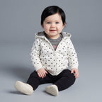 Bebé sonriente con conjunto EmpiBy de chaqueta blanca con corazones, body a rayas y legging negro sobre fondo gris.