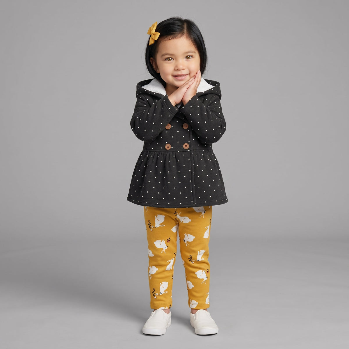 Niña pequeña con conjunto EmpiBy de chaqueta negra con lunares, body blanco y pantalón mostaza con estampado de conejos