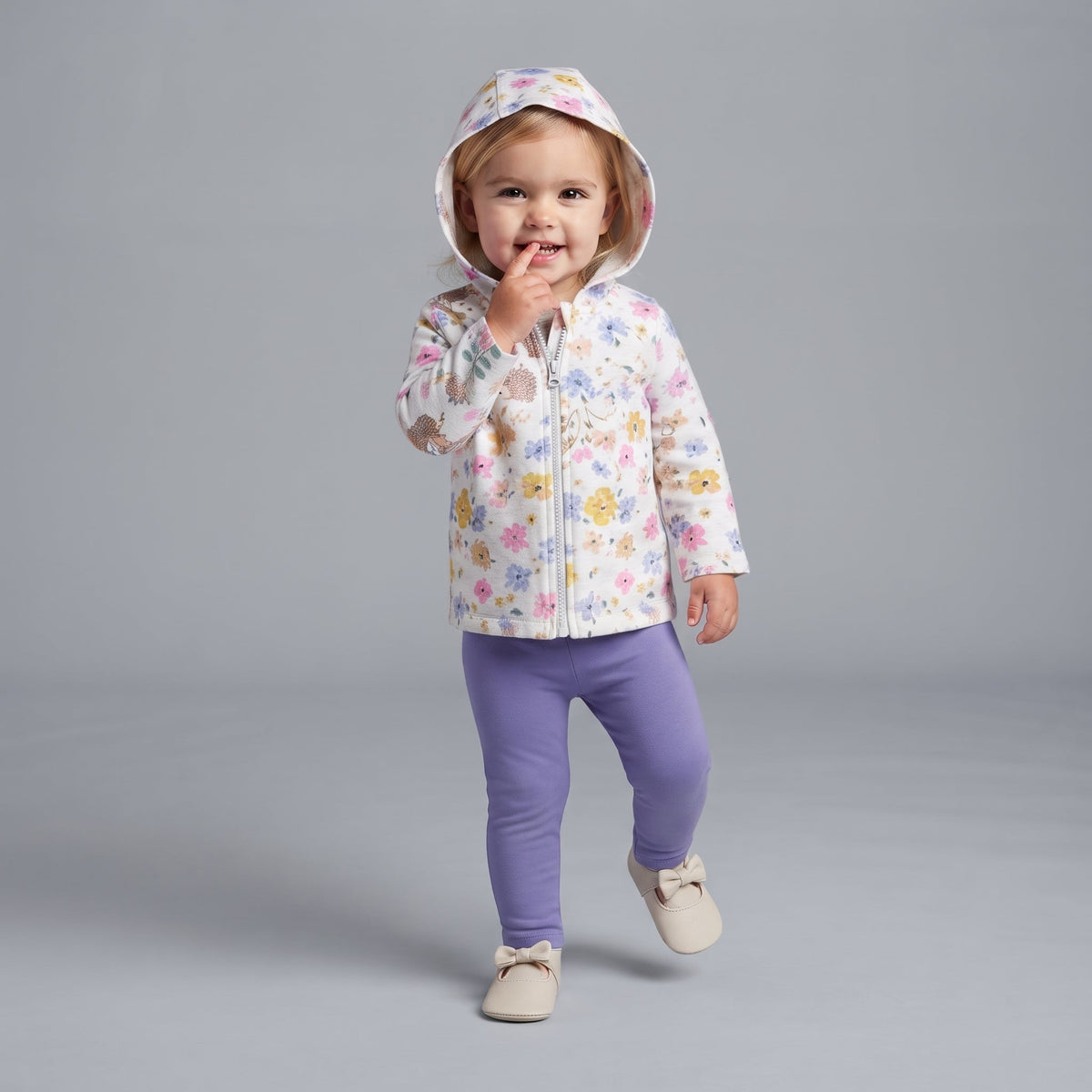 Niña pequeña con conjunto EmpiBy de chaqueta blanca floral con capucha, body gris y leggings morados.