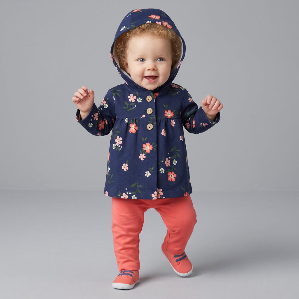 Bebé niña sonriente vistiendo conjunto EmpiBy de chaqueta azul marino con flores, body blanco y pantalón rosa salmón.