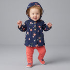 Bebé niña sonriente vistiendo conjunto EmpiBy de chaqueta azul marino con flores, body blanco y pantalón rosa salmón.