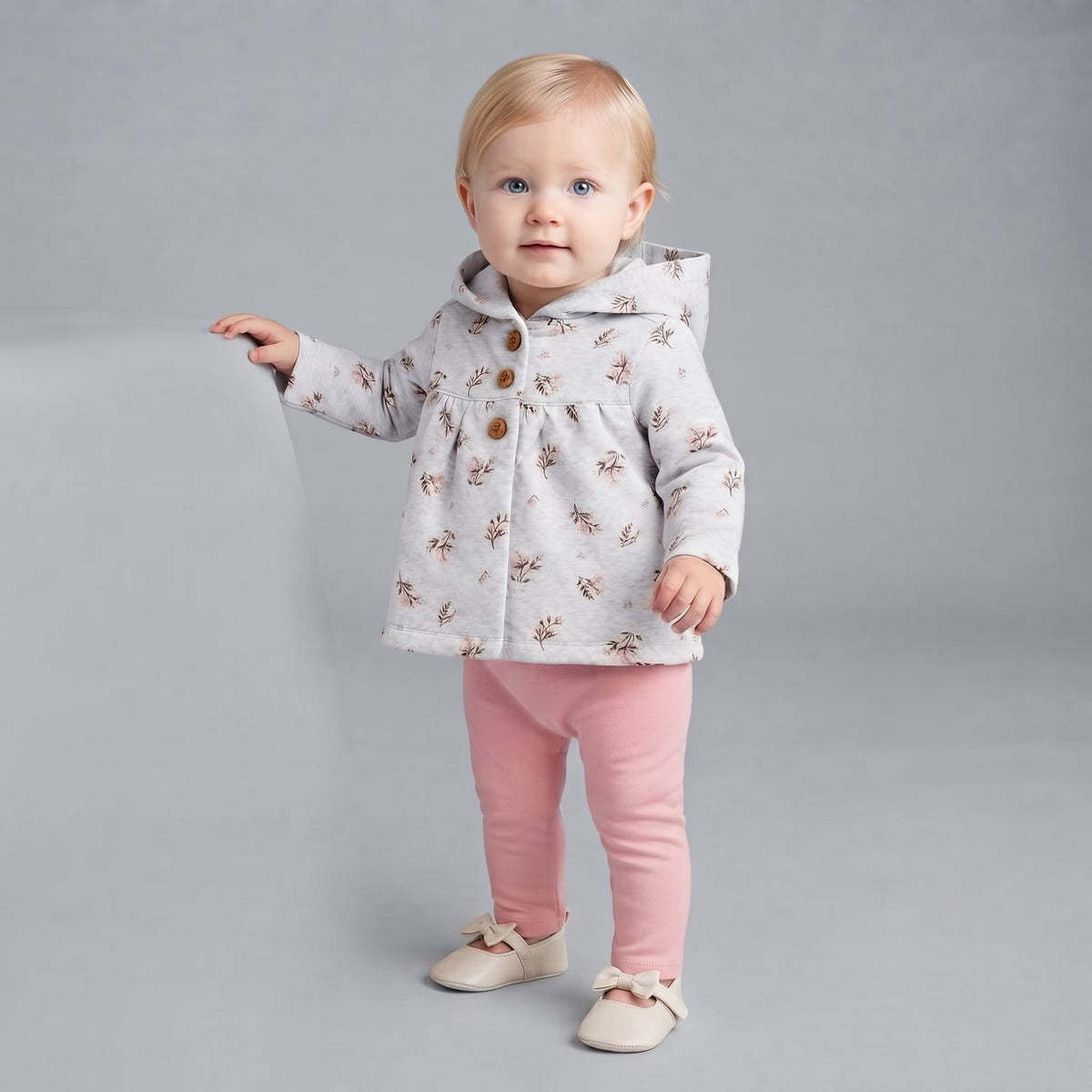 Bebé niña vistiendo conjunto EmpiBy de chaqueta gris con flores, legging rosa y zapatitos sobre fondo gris