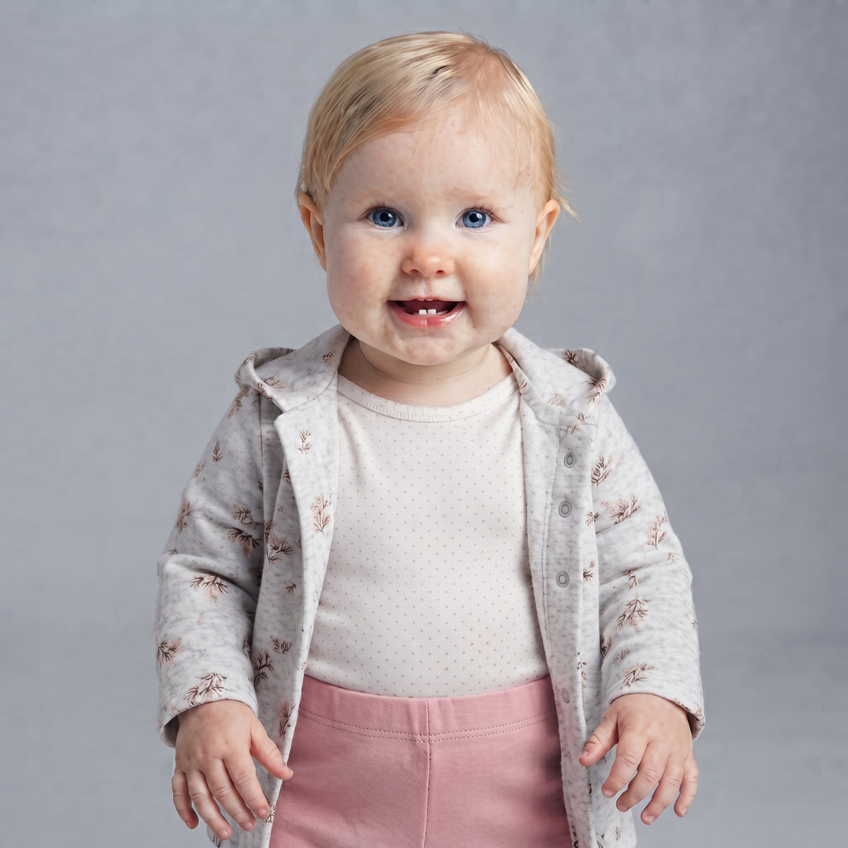 Bebé niña vistiendo conjunto EmpiBy de 3 piezas: chaqueta gris con flores, body de lunares y legging rosa suave.