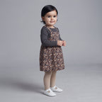 Niña pequeña con conjunto EmpiBy de vestido peto estampado leopardo, camiseta gris acanalada y medias beige.