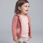 Niña sonriente con conjunto EmpiBy de chaqueta rosa con lunares, body marfil y pantalón estampado de manzanas.