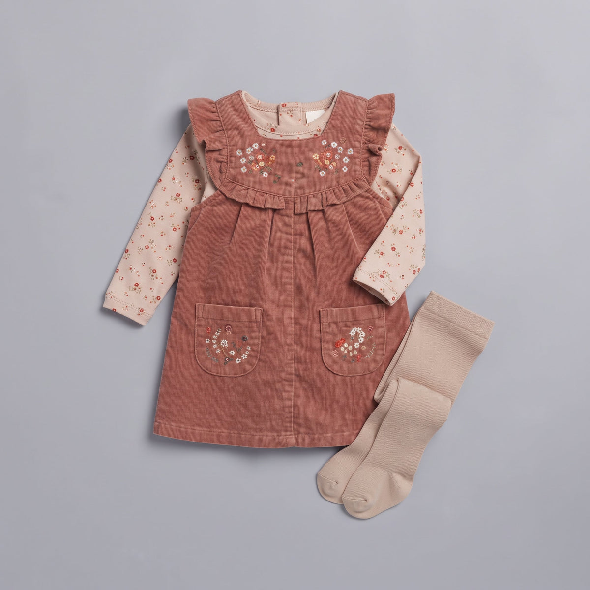 Conjunto EmpiBy de 3 piezas para bebé niña con vestido de pana terracota, blusa floral y medias beige de algodón.