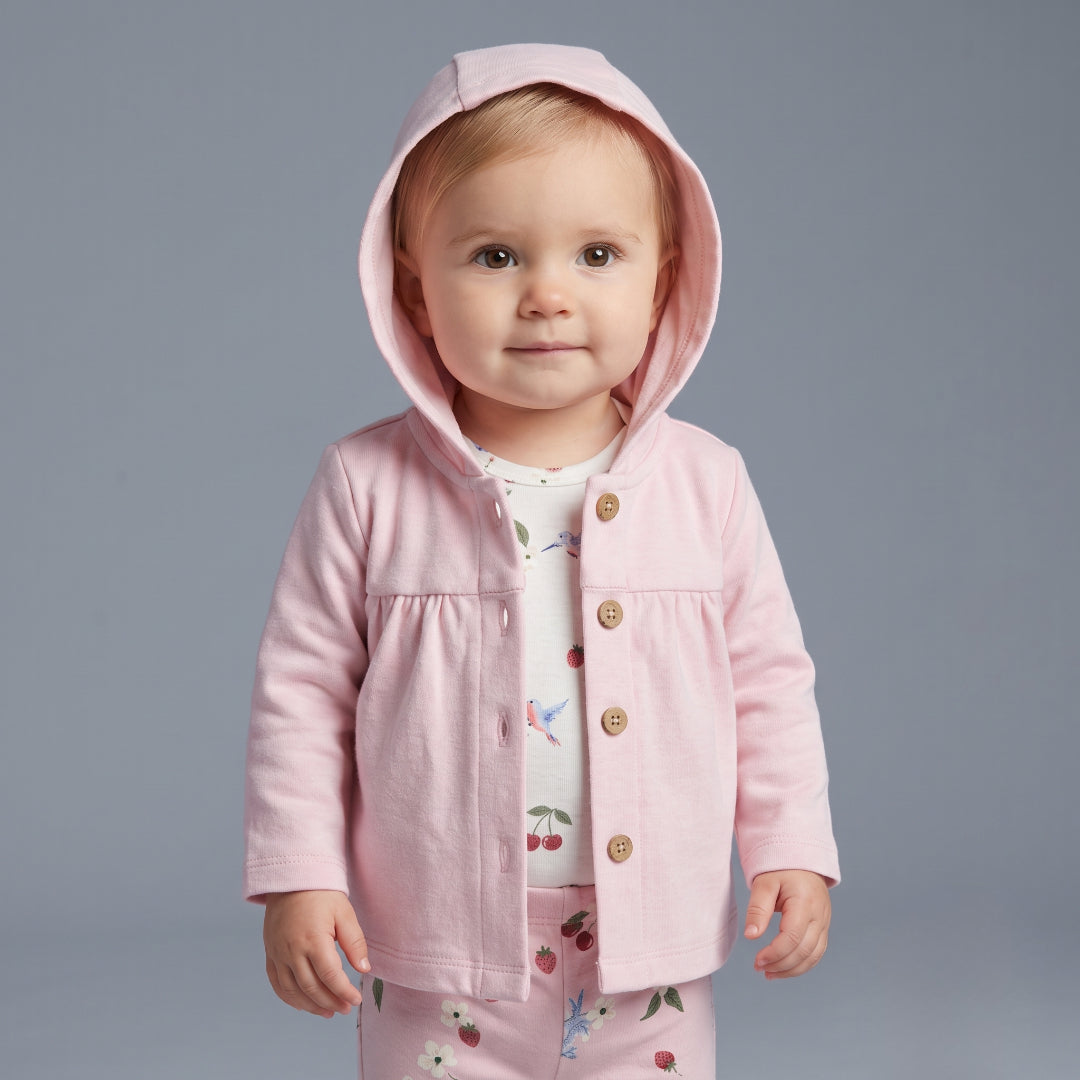 Bebé niña vistiendo conjunto EmpiBy de tres piezas: chaqueta rosa con capucha, body blanco estampado y legging floral.