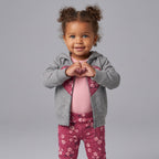 Niña pequeña con conjunto EmpiBy de 3 piezas: chaqueta gris con corazón, body rosa y legging floral frambuesa.