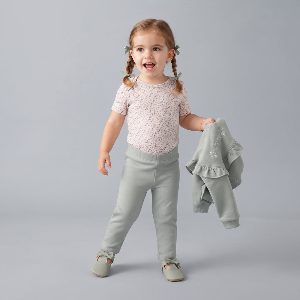 Niña pequeña con conjunto EmpiBy de tres piezas: body floral, pantalón verde salvia y sudadera con volantes.