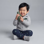 Bebé niño sonriente con conjunto EmpiBy de 3 piezas: chaqueta gris con dinosaurio, body a rayas y pantalón estampado.