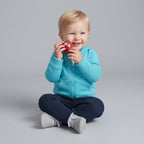 Bebé sonriente con conjunto EmpiBy de chaqueta turquesa con capucha, pantalón azul y coche de juguete rojo