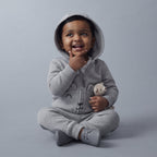 Bebé sonriente con conjunto EmpiBy de tres piezas gris, chaqueta con capucha de osito y pantalón cómodo