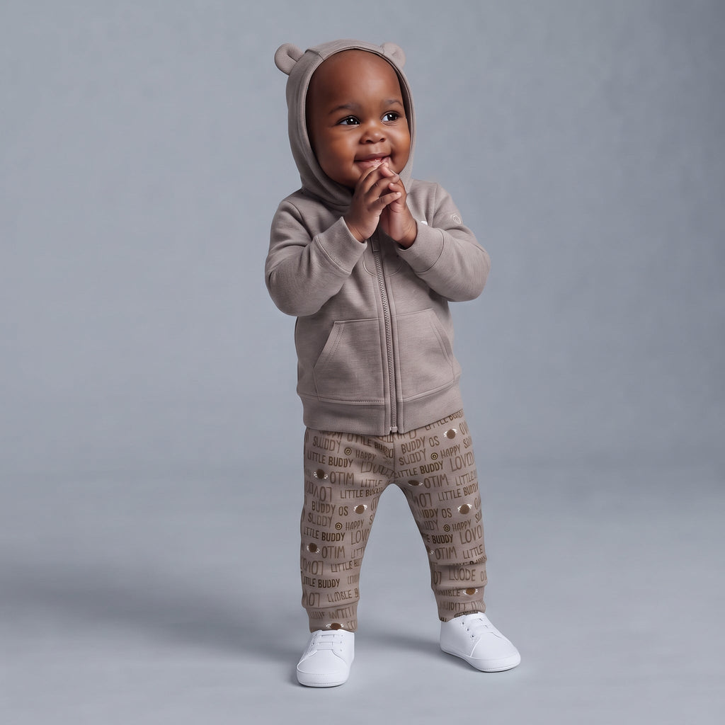 Bebé con conjunto EmpiBy de 3 piezas: chaqueta con capucha y orejitas, pantalón estampado y zapatillas blancas.