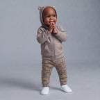 Bebé con conjunto EmpiBy de 3 piezas: chaqueta con capucha y orejitas, pantalón estampado y zapatillas blancas.