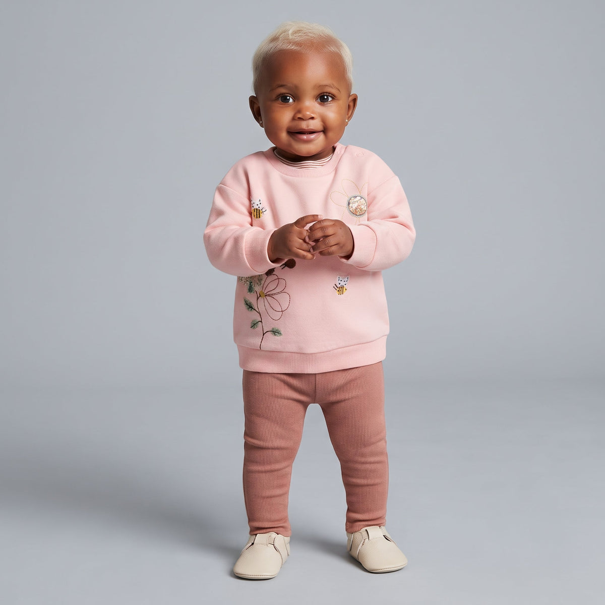 Bebé sonriente con conjunto EmpiBy de sudadera rosa con flores bordadas y leggings acanalados color terracota