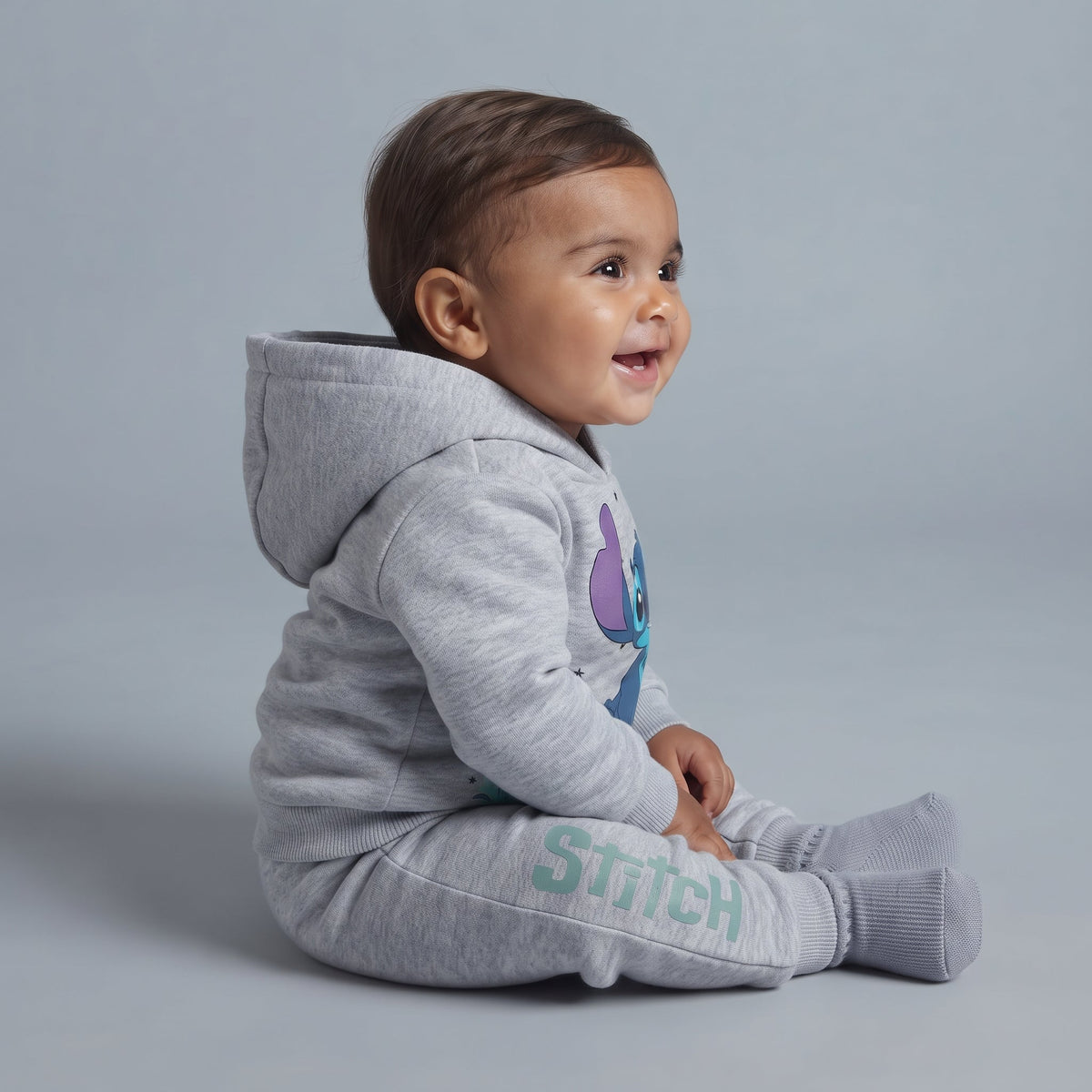 Bebé sonriente con conjunto EmpiBy de sudadera y jogger gris jaspeado con estampado de Stitch y capucha.