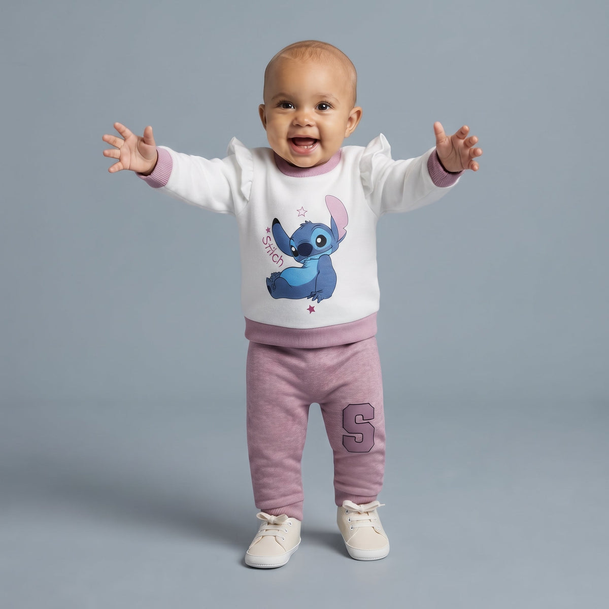 Bebé feliz vistiendo conjunto EmpiBy de dos piezas con sudadera blanca de Stitch y pantalón jogger malva