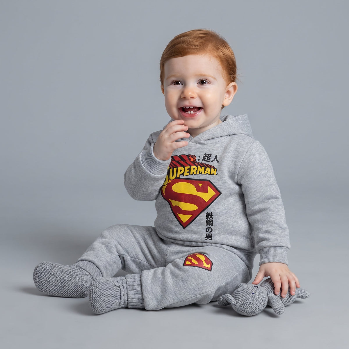 Bebé sonriente vistiendo conjunto EmpiBy de dos piezas gris de Superman con sudadera con capucha y pantalón jogger