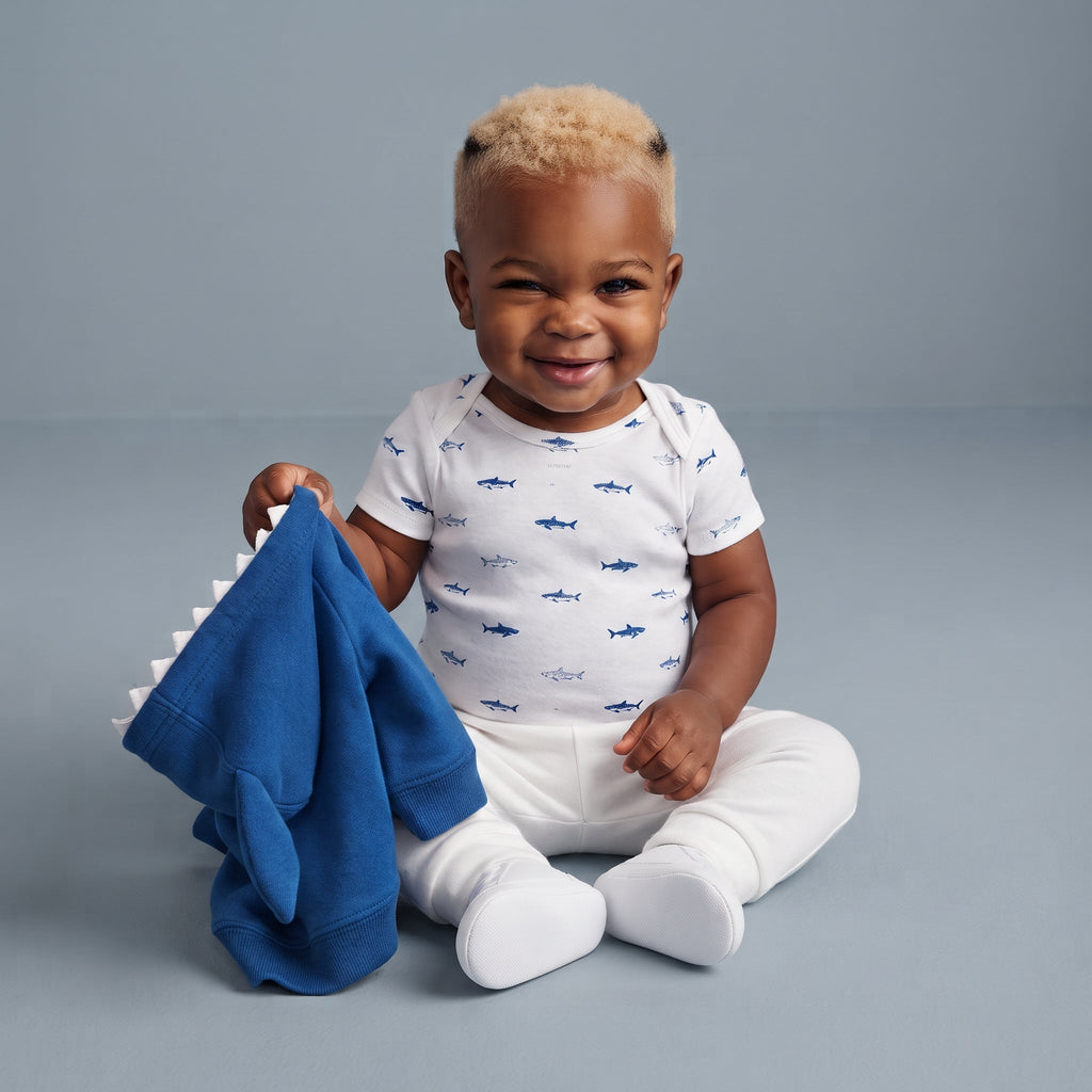 Bebé sonriente con conjunto EmpiBy de 3 piezas: body de tiburones, pantalón blanco y chaqueta azul con capucha.