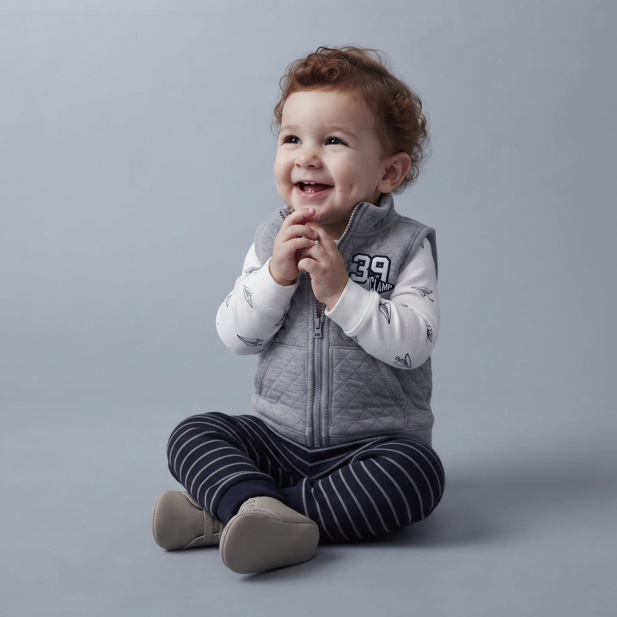 Bebé sonriente vistiendo conjunto EmpiBy de 3 piezas: chaleco gris acolchado, body blanco estampado y pantalón a rayas