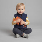 Bebé con conjunto EmpiBy de 3 piezas: chaleco azul marino, body a rayas y pantalón gris, sosteniendo un mamut naranja.