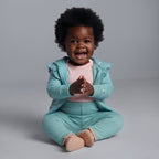 Bebé sonriente con conjunto EmpiBy de tres piezas: chaqueta azul menta, body rosa y pantalón floral a juego.