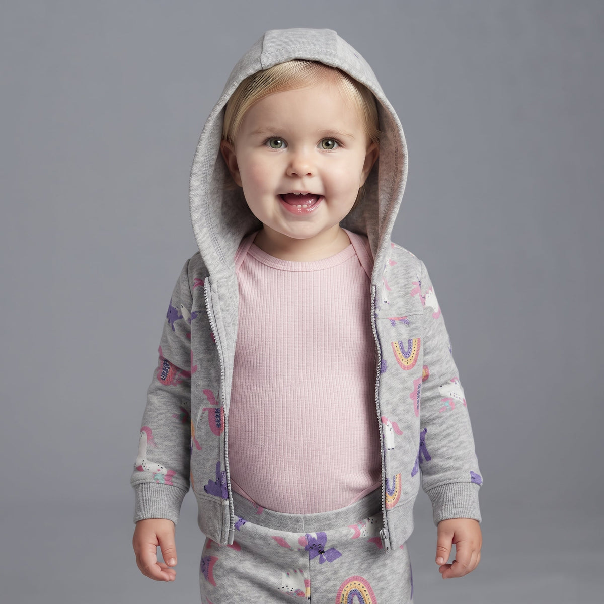 Bebé niña con conjunto EmpiBy de tres piezas: chaqueta gris con capucha, body rosa y pantalón con estampado unicornio