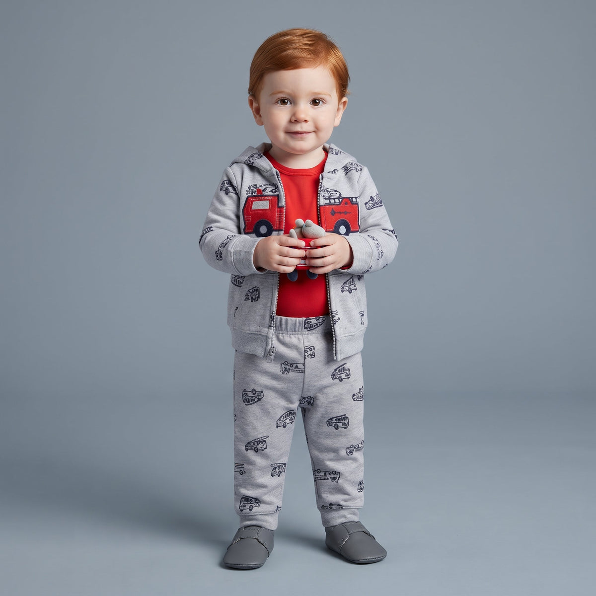 Niño pequeño con conjunto EmpiBy de 3 piezas: chaqueta gris con camión de bomberos, body rojo y pantalón estampado.