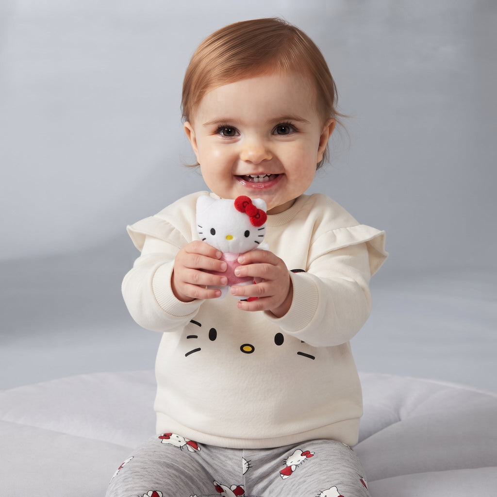 Bebé sonriente con conjunto EmpiBy de Hello Kitty: sudadera marfil con volantes y leggings grises estampados.