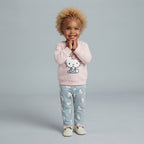 Niña pequeña sonriendo con conjunto EmpiBy de suéter rosa Hello Kitty y pantalón gris estampado, estilo casual.