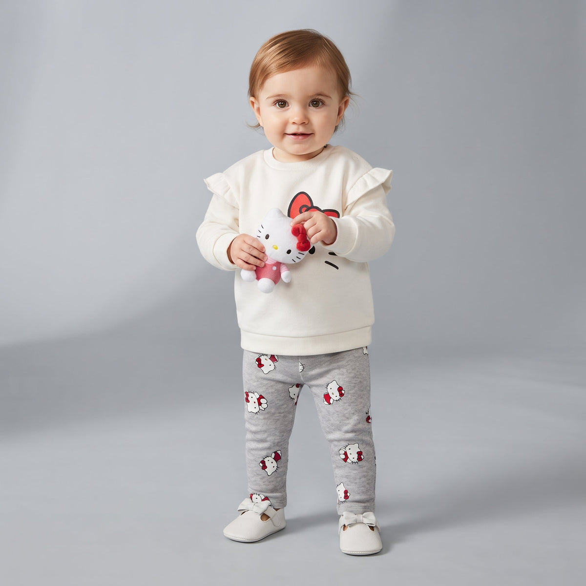 Bebé con conjunto EmpiBy de dos piezas: sudadera marfil con volantes y legging gris estampado de Hello Kitty