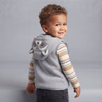 Niño pequeño con chaleco gris EmpiBy con capucha de mapache, body de rayas y pantalón gris sobre fondo neutro