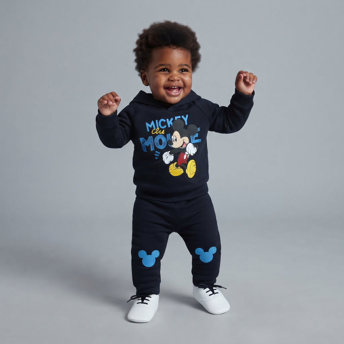 Bebé sonriente vistiendo conjunto EmpiBy de sudadera con capucha y jogger azul marino con estampado de Mickey Mouse