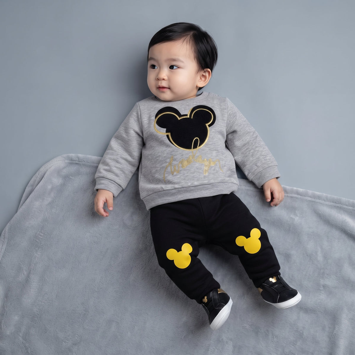 Bebé vistiendo conjunto EmpiBy de dos piezas con sudadera gris de Mickey Mouse y pantalón jogger negro con detalles