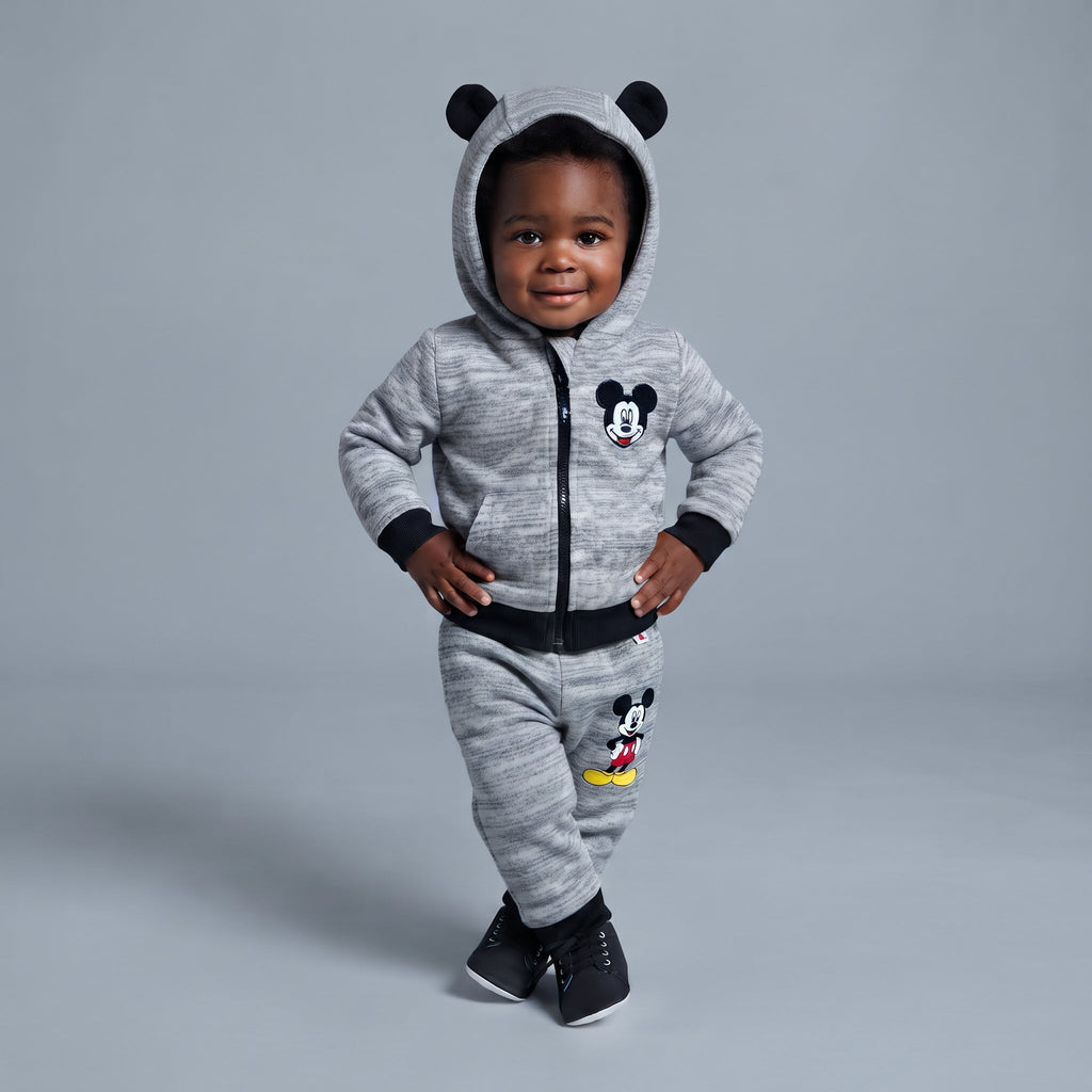 Bebé sonriente vistiendo conjunto EmpiBy de Mickey Mouse gris jaspeado con sudadera de orejitas y pantalón jogger