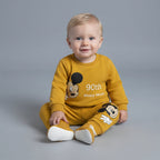 Bebé sonriente con conjunto EmpiBy mostaza de dos piezas de Mickey Mouse con estampado conmemorativo del 90 aniversario