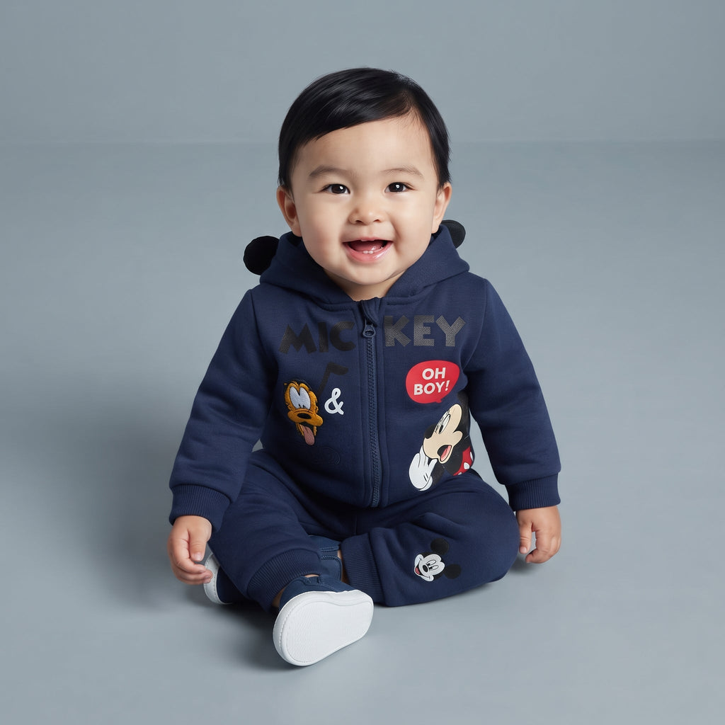 Bebé sonriente con conjunto EmpiBy de Mickey Mouse azul marino, chaqueta con capucha y orejas 3D y pantalón jogger.