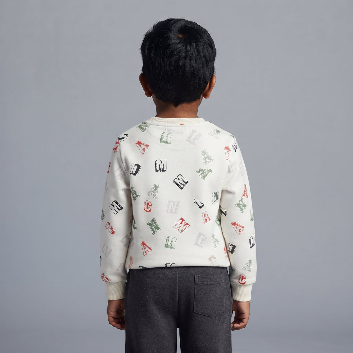 Niño de espaldas vistiendo conjunto EmpiBy con buzo blanco estampado de letras y pantalón gris oscuro