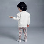 Niña pequeña vistiendo conjunto EmpiBy de sudadera blanca con volantes y leggings estampados de flores