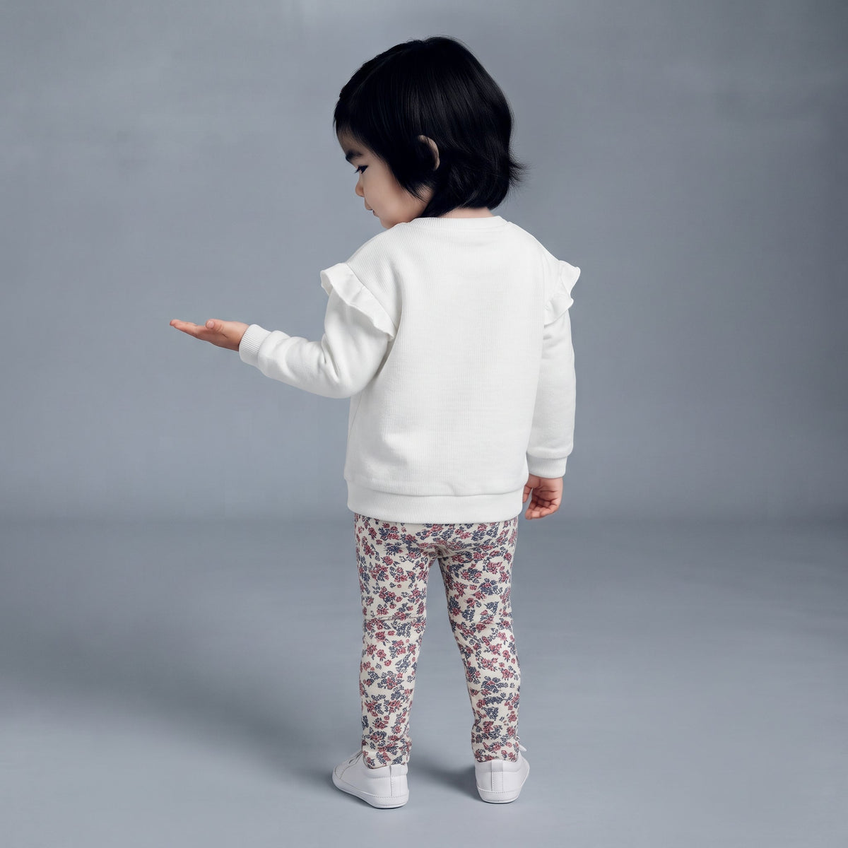 Niña pequeña vistiendo conjunto EmpiBy de sudadera blanca con volantes y leggings estampados de flores