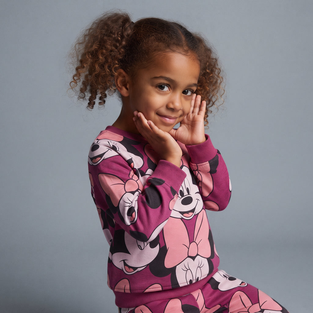 Niña sonriente vistiendo conjunto EmpiBy de dos piezas fucsia con estampado de Minnie Mouse y cuello redondo