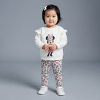 Niña pequeña con conjunto EmpiBy de sudadera blanca con volantes y estampado de Minnie Mouse y legging floral