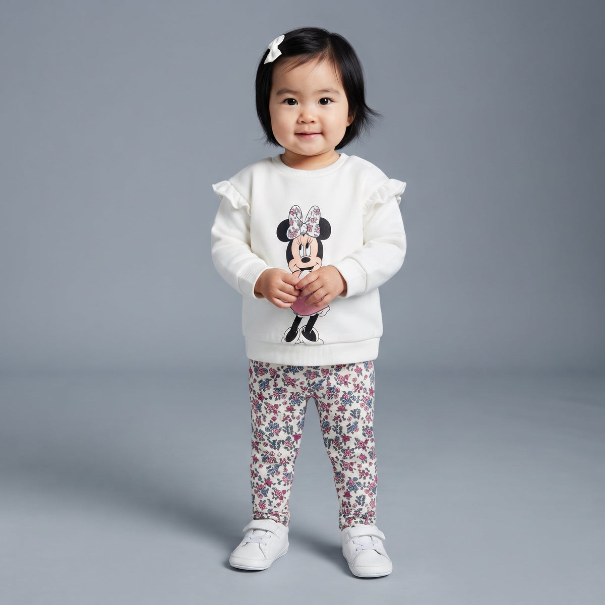 Niña pequeña con conjunto EmpiBy de sudadera blanca con volantes y estampado de Minnie Mouse y legging floral