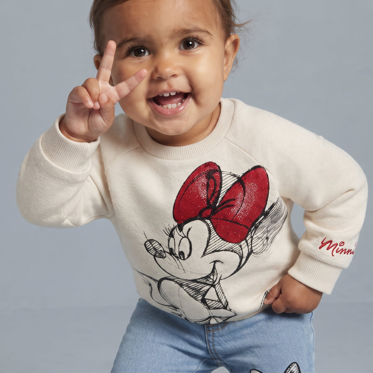 Niña sonriente vistiendo conjunto EmpiBy de suéter crema con estampado de Minnie Mouse y pantalón de mezclilla azul